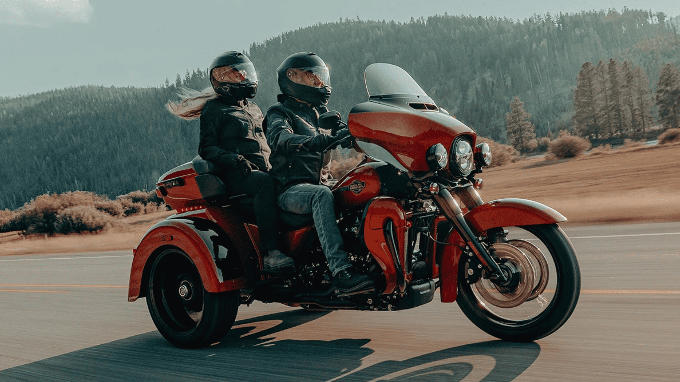 Two riders on a Trike Harley-Davidson® motorcycle cruising down a road, showcasing the MY2025 Harley-Davidson® lineup near Orlando, FL. Available at Space Coast Harley-Davidson® 