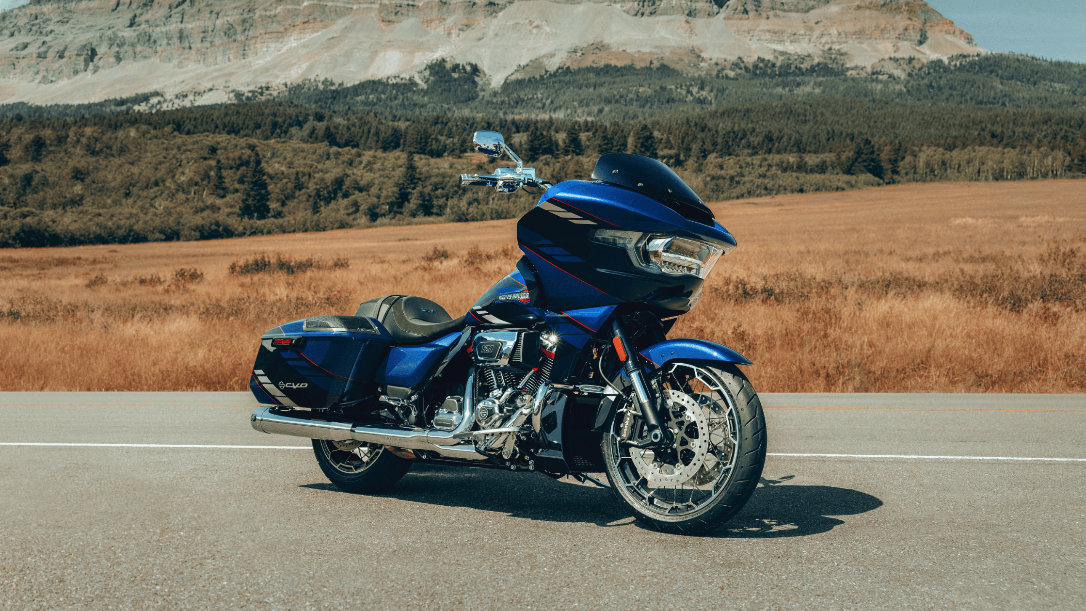 A blue 2025 Harley-Davidson® CVO™ Road Glide® motorcycle parked on a road with mountains, located ne…